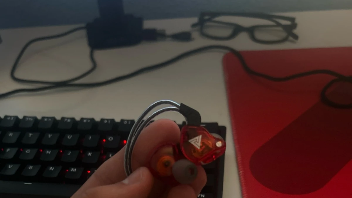 Teste prático do fone intra-auricular QKZ AK6 em mãos sobre mesa de setup gamer com teclado mecânico